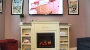 A living room with a white fireplace, a red ottoman, and a blue sofa. - Pink Fridge! Condo in Downtown Whitefish (Whitefish)