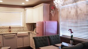 A kitchen with white cabinets, a pink refrigerator, and a dining area with a table and chairs. - Pink Fridge! Condo in Downtown Whitefish (Whitefish)