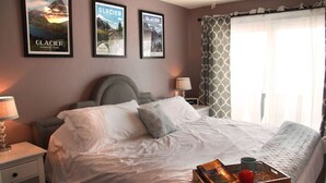 A neatly made bed with white linens, a tray with a book and a mug, and framed posters on the wall. - Pink Fridge! Condo in Downtown Whitefish (Whitefish)