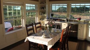 A dining area with a table set for four, large windows with a view, and a kitchen area with cabinets and a countertop. - AUBURN COTTAGE POOL HOUSE, SPA AND GROUNDS G & Christmas Now Open 5 day min (Auburn)