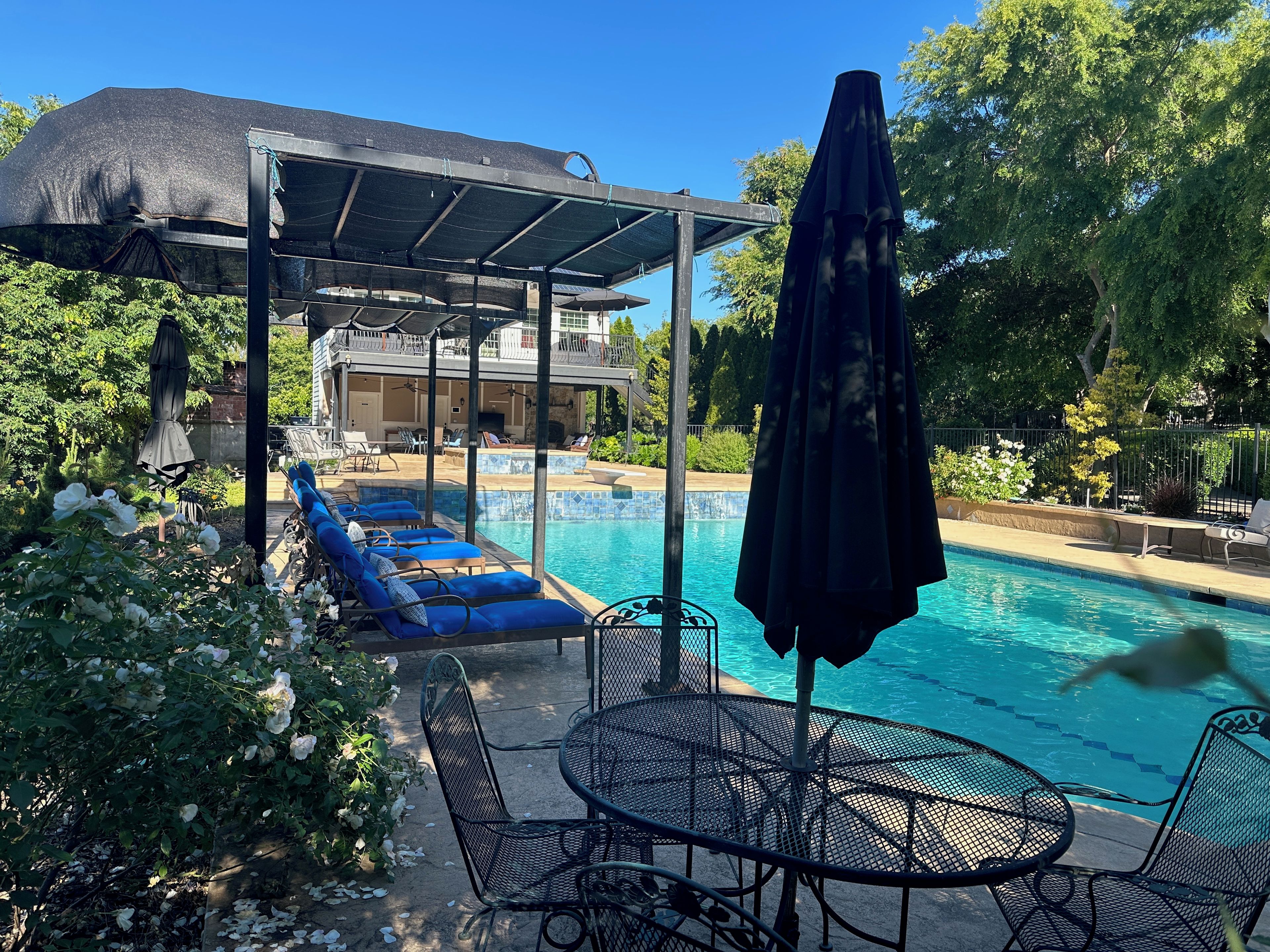 An outdoor pool area with lounge chairs, a table, and a covered seating area.