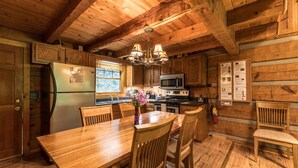 A wooden cabin kitchen with a wooden table, chairs, a refrigerator, a stove, and a microwave. - Fireplace, firepit, hot tub, minutes from Ski Resort - Low rates, no inflation ! (Gatlinburg)