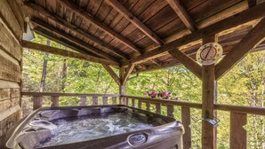 A hot tub under a wooden gazebo with a wooden railing, surrounded by trees. - Fireplace, firepit, hot tub, minutes from Ski Resort - Low rates, no inflation ! (Gatlinburg)