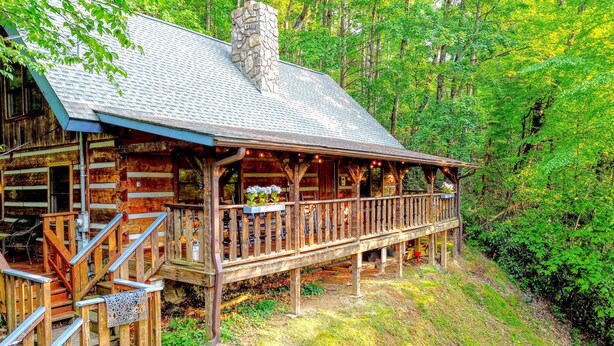 A rustic log cabin with a balcony, surrounded by lush greenery. - Fireplace, firepit, hot tub, minutes from Ski Resort - Low rates, no inflation ! (Gatlinburg)