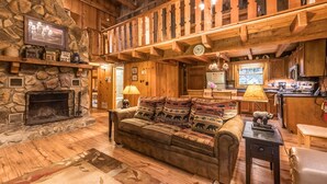 A cozy cabin interior with a stone fireplace, wooden furniture, a dining area, and a kitchen. - Fireplace, firepit, hot tub, minutes from Ski Resort - Low rates, no inflation ! (Gatlinburg)