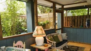 Une pièce chaleureuse avec un banc en bois, une petite table avec une lampe et une vue sur la verdure à l’extérieur.