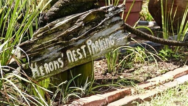 Un panneau en bois portant l’inscription « Parking réservé aux héros », en partie masqué par le feuillage.