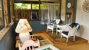 Une pièce chaleureuse avec un plancher en bois, une chaise blanche, une petite table avec une lampe et une fenêtre donnant sur un paysage verdoyant.