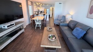 Un salon moderne doté d’un téléviseur à écran plat, d’un coin repas avec des chaises, d’un canapé et d’une table basse.