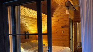 A cozy wooden cabin room with two beds, a ceiling fan, and a window with curtains. - Heated Pool, Hot Tub, Fenced for Dogs, Views, Walk to Cafe, EV Charger (Leavenworth)