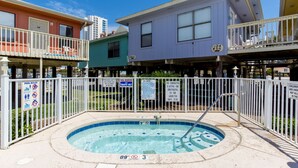 A pool area with a hot tub, surrounded by a white fence, and adjacent colorful buildings. - 2 Bedroom, Across the street from the beach! & Pup-Friendly! (Gulf Shores)