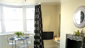 A living room with a sofa, a dining table with chairs, a TV, a fireplace, and a window with curtains. - Romantic with Sea View Sleeps 2-4 (Brighton)