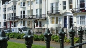 A row of white terraced houses with balconies, a clear sky, and a green lawn in the foreground. - Romantic with Sea View Sleeps 2-4 (Brighton)