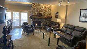 A living room with a stone fireplace, leather sofas, and a glass coffee table.