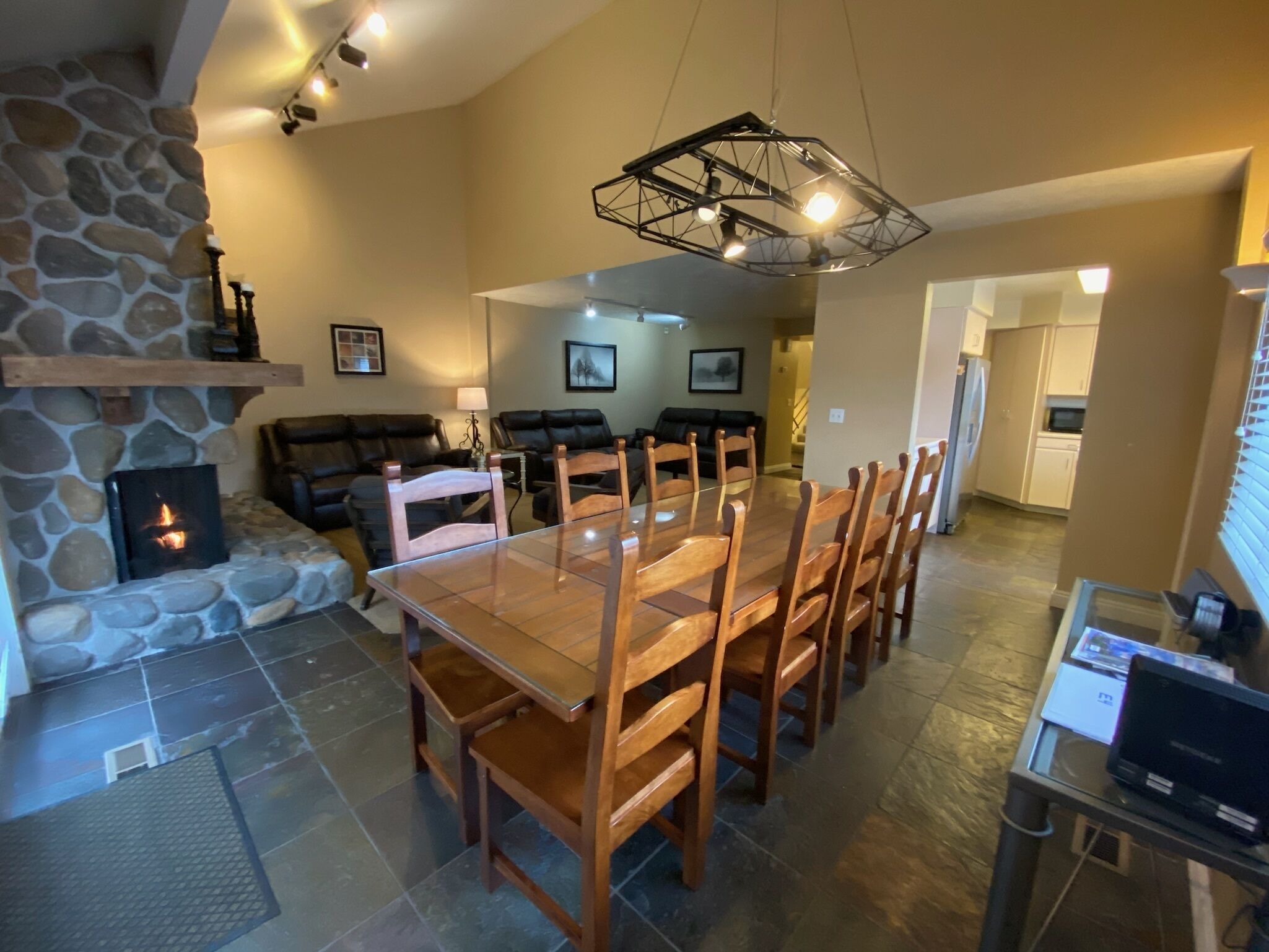 A spacious living area with a stone fireplace, a dining table with wooden chairs, a black leather sofa, and a modern pendant light.