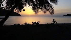 Atardecer sobre un mar tranquilo con siluetas de palmeras y barcos a lo lejos.