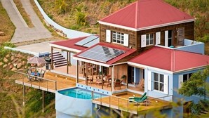 Una casa moderna con techo rojo, piscina y terraza con mobiliario exterior.