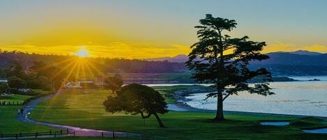 A golf course with a view of the ocean and mountains during sunset.