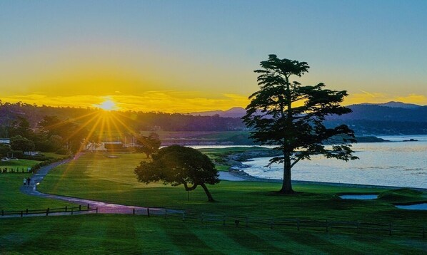 Un parcours de golf offrant une vue sur l’océan et les montagnes au coucher du soleil.