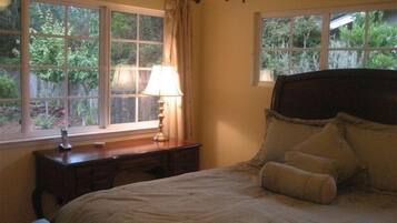 Une chambre à coucher avec un lit, une table de chevet, une lampe et deux fenêtres avec des rideaux.
