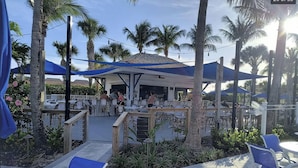 An outdoor patio area with tables and chairs, surrounded by palm trees and a covered seating area. - Luxury Ocean Village Beach Condo with 5 Star Reviews with Wifi and all Extras (Fort Pierce)