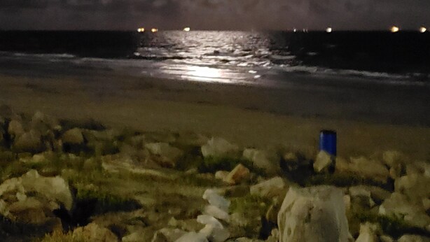 A nighttime beach scene with a rocky foreground, a calm sea, and a bright moon in the sky. - VRBO 184287 Book Group trip Late Spring/Summer! We're Booked (Galveston)