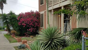 A two-story house with a balcony, surrounded by a garden with various plants and flowers. - VRBO 184287 Book Group trip Late Spring/Summer! We're Booked (Galveston)