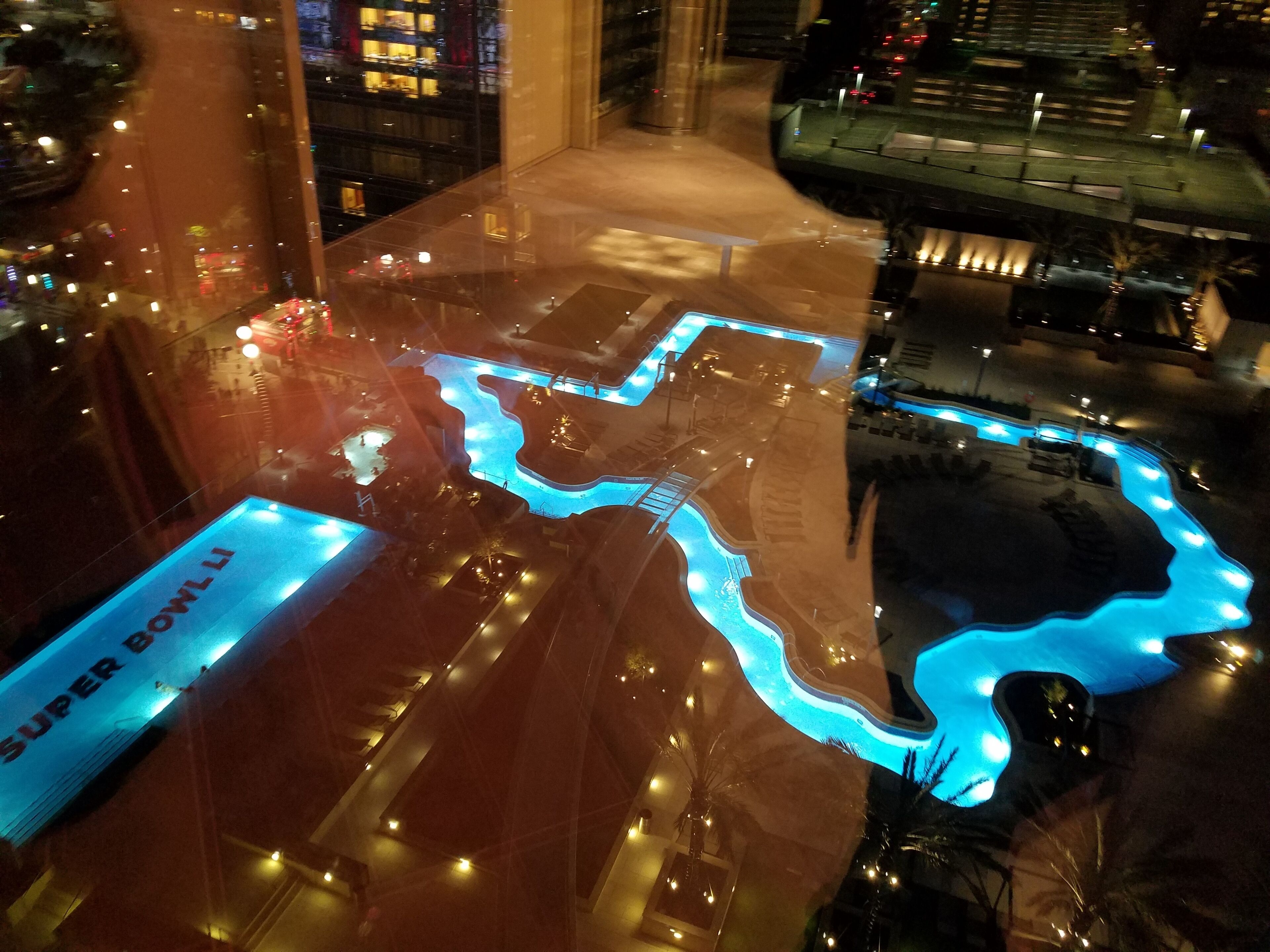 Une vue aérienne d’un hôtel avec une piscine, une enseigne indiquant « SUPER BOWL LI », et un grand bâtiment en arrière-plan.