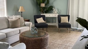 Una sala de estar con una pared azul claro, un ventilador de techo blanco, un sofá, dos sillones, una mesa de centro y una planta en maceta.