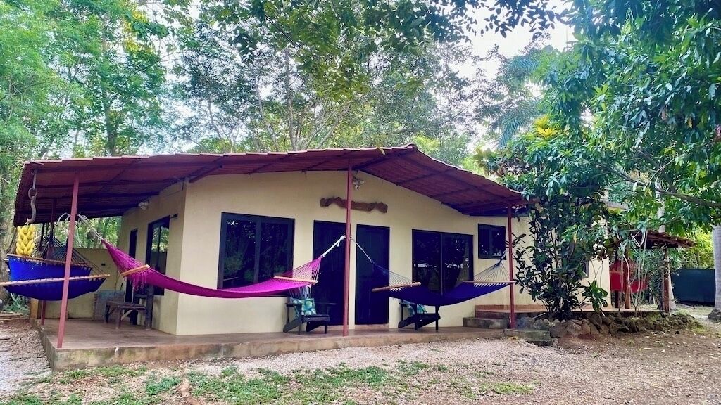 A single-story building with a covered porch, two hammocks, and a small outdoor seating area.