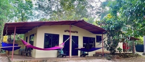 A single-story building with a covered porch, two hammocks, and a small outdoor seating area.