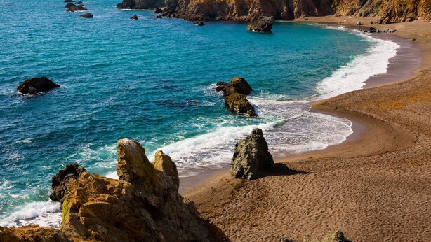 Eine Küstenlandschaft mit Felsformationen und einem Sandstrand.