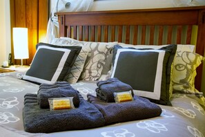 Un lit bien fait, avec une couvre-lit à motifs floraux, une tête de lit en bois et une lampe de chevet.