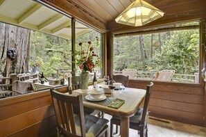 Un coin repas avec une table dressée pour deux personnes, entouré de murs en bois et de grandes fenêtres donnant sur la forêt.