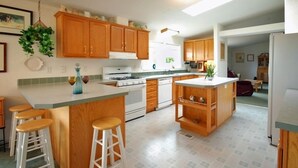 Una cocina con armarios de madera, una isla central con taburetes, una estufa y un refrigerador.