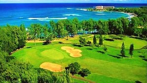 A golf course with a view of the ocean and a resort building in the background.