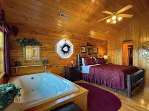 Une chambre dans une cabane en bois, avec un grand lit, une baignoire et un ventilateur de plafond.