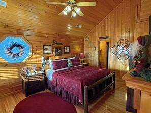 A wooden cabin bedroom with a bed, nightstands, a ceiling fan, and wall decorations. - Gorgeous Mtn Sunset View/NO PETS/Closest 2 Dollywd/15 minutes 2 GSMNP/Gatlinburg (Pigeon Forge)