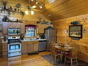 A wooden interior with a kitchen featuring stainless steel appliances, a dining table with chairs, and a ceiling fan. - Gorgeous Mtn Sunset View/NO PETS/Closest 2 Dollywd/15 minutes 2 GSMNP/Gatlinburg (Pigeon Forge)
