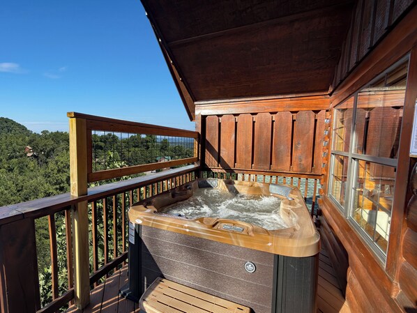 A wooden deck with a hot tub and a view of a forested area.