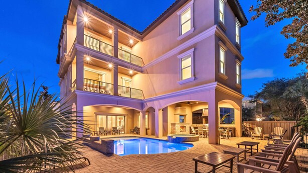Una casa de varios pisos con piscina, mobiliario exterior y un patio cubierto.