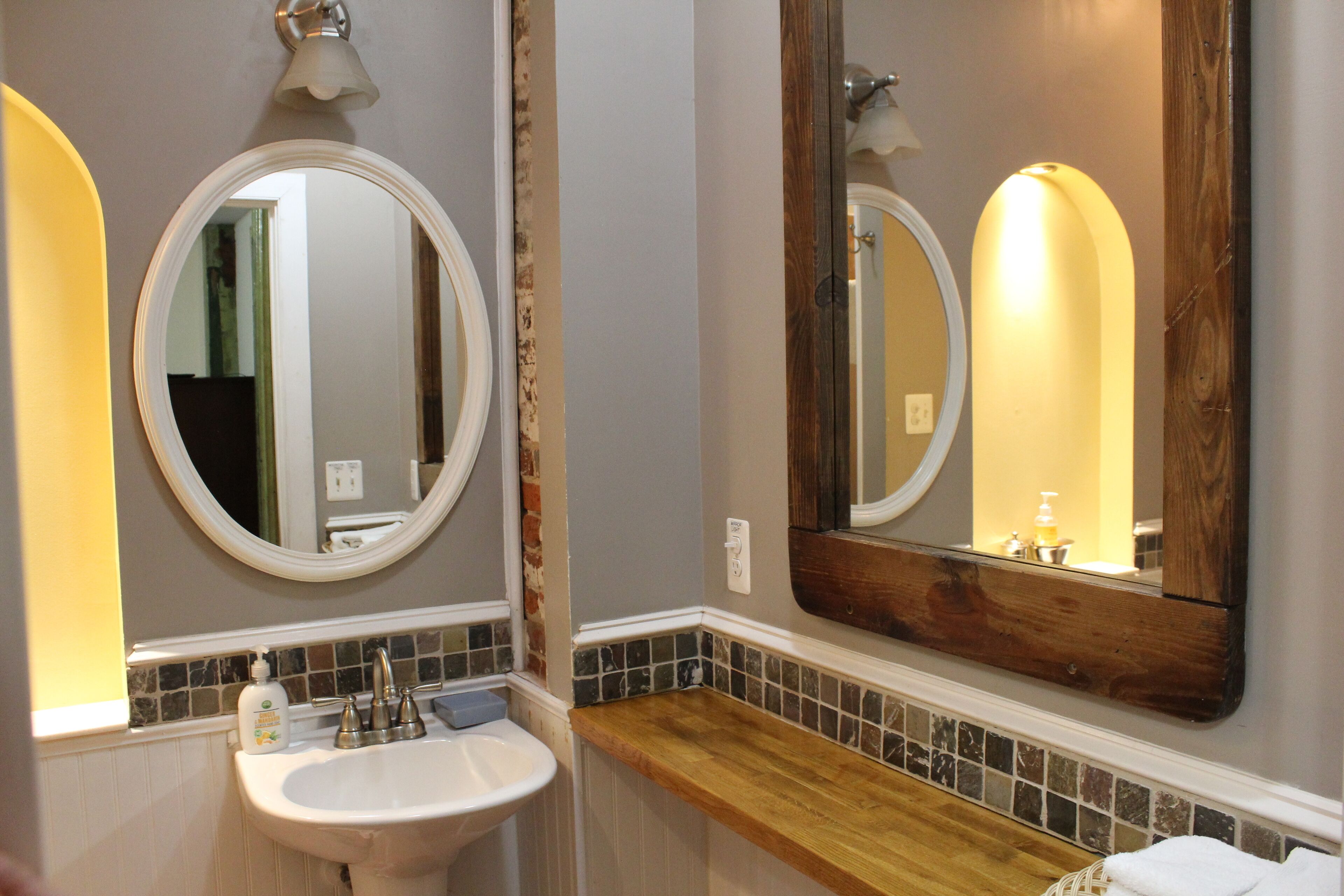 Une salle de bain avec un lavabo blanc, un meuble-lavabo en bois et deux miroirs encadrés en bois.