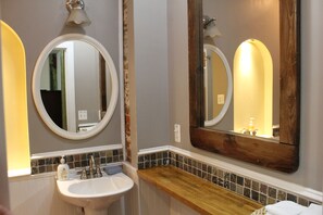 A bathroom with a white sink, a wooden vanity, and two mirrors with wooden frames. - Cozy Fells Point Gem / In The Heart of Fells Point (Baltimore)