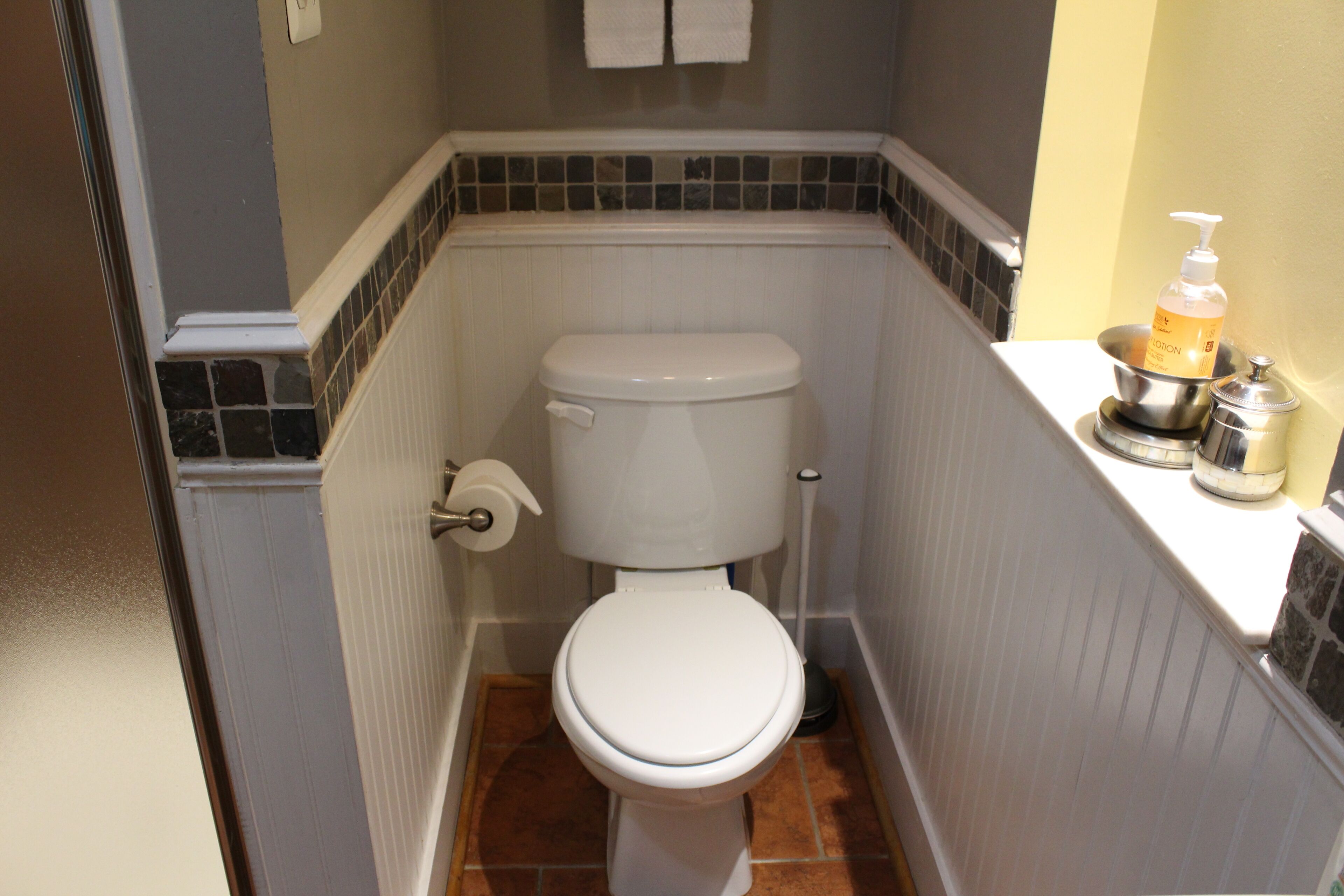 A small bathroom with a white toilet, a toilet paper holder, and a soap dispenser on the counter.