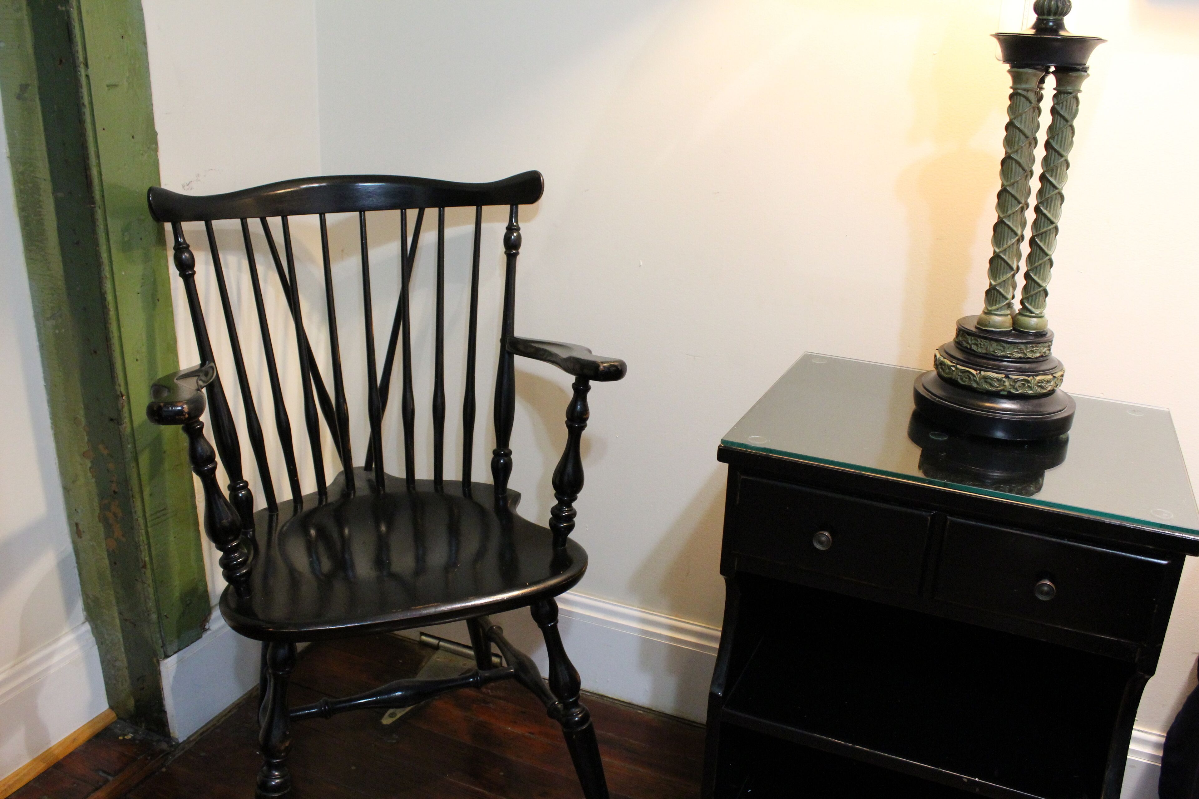 Una silla de madera negra con respaldo y reposabrazos curvados, ubicada junto a un aparador negro con cajones.