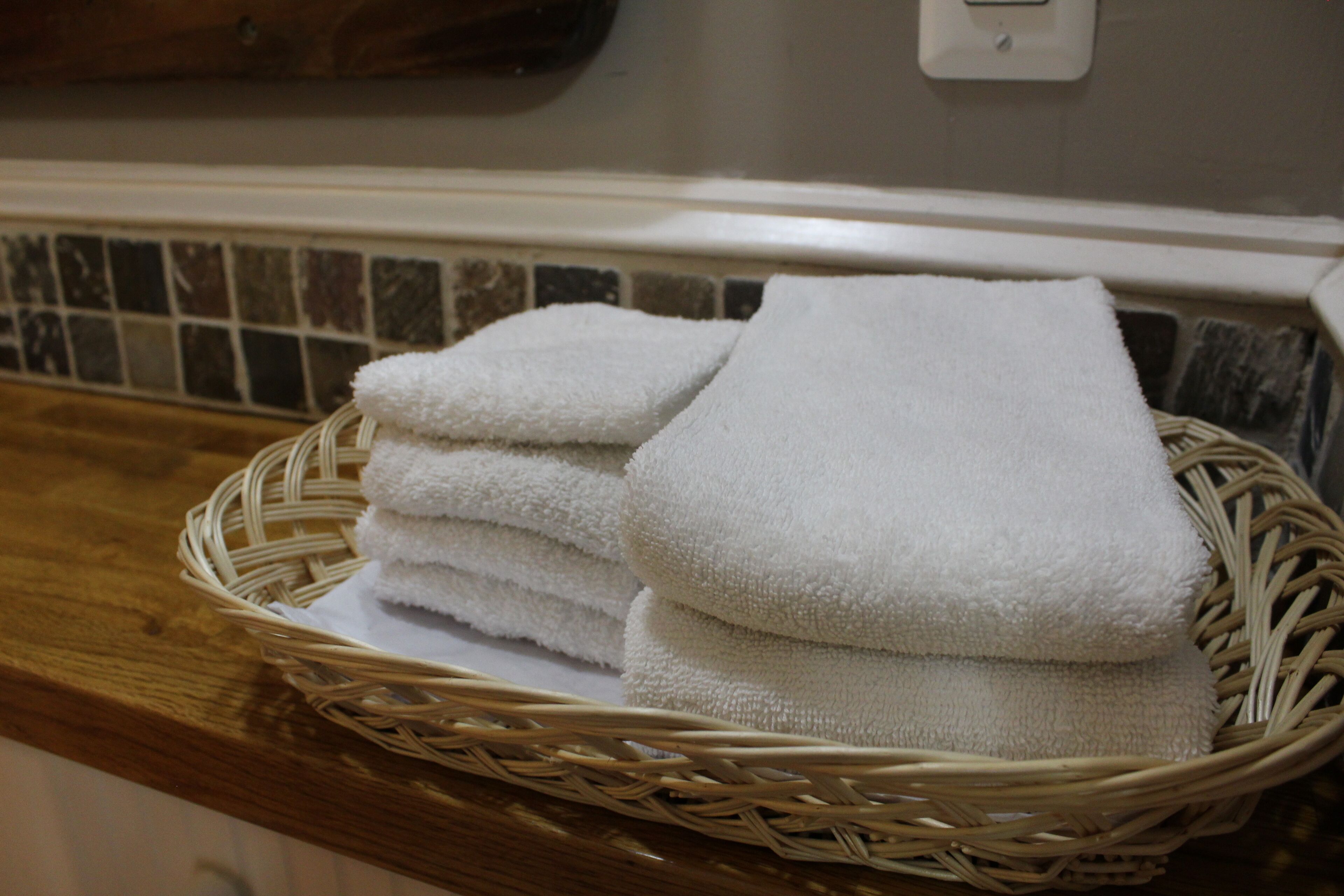 A wicker basket filled with neatly folded white towels on a wooden countertop.