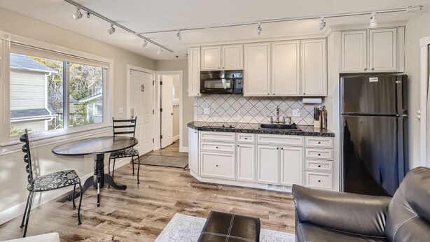 A modern kitchen with white cabinets, a black refrigerator, and a dining area with a table and chairs. - Downtown Boulder Guest House for 2 guests (Boulder)