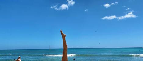 Une scène de plage, avec un ciel dégagé et une personne pratiquant une posture de yoga sur une serviette.