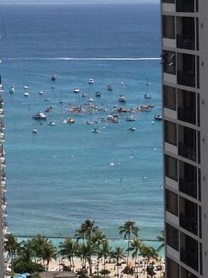 Vista de una playa con numerosos barcos, palmeras y un edificio de varios pisos.