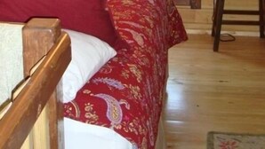 A cozy attic bedroom with a wooden ceiling, a large window, a bed with red bedding, and two bedside lamps. - Cozy Eagles Nest Cabin Above the River! 6 Blocks from Yellowstone Park  (Gardiner)